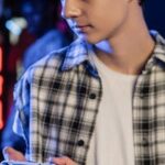 A teenage boy focused while holding a game controller in a dimly lit room.